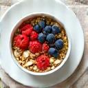 Tazón de granola saludable con frutas frescas y bayas, con un vaso de leche de almendras.