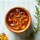 Cápsulas de vitaminas y hierbas en cuencos de madera, con una planta verde en el fondo.